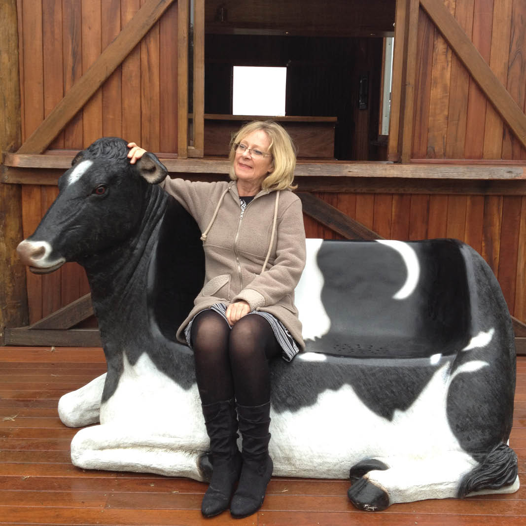 Natureworks Australia Cowch - Friesian cow settee-120020- shown outside in front of a barn - with lady sitting on bench
