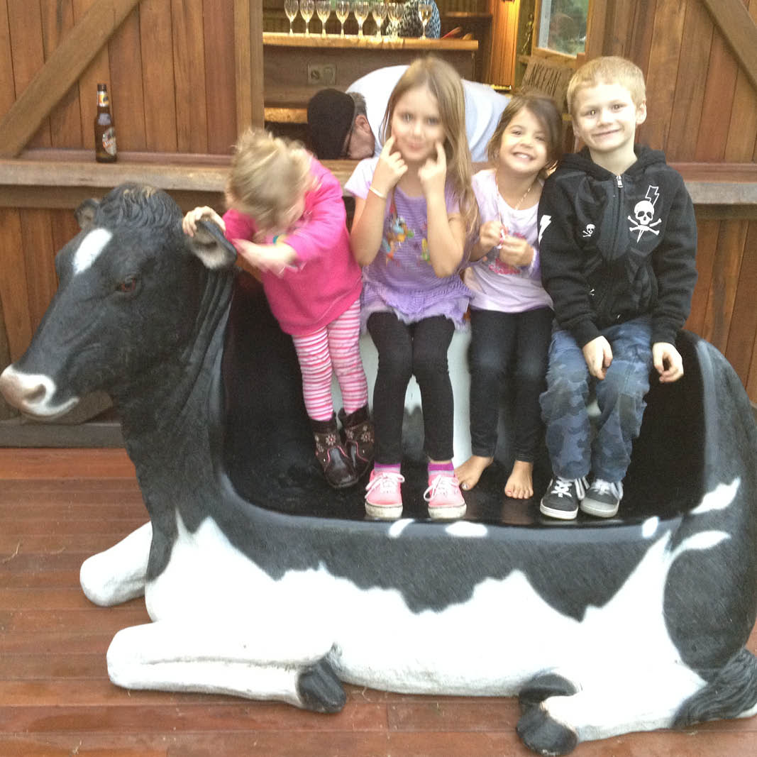 Natureworks Australia Cowch - Friesian cow settee-120020- shown outside in front of a barn - with a bunch of children standing on cowch settee
