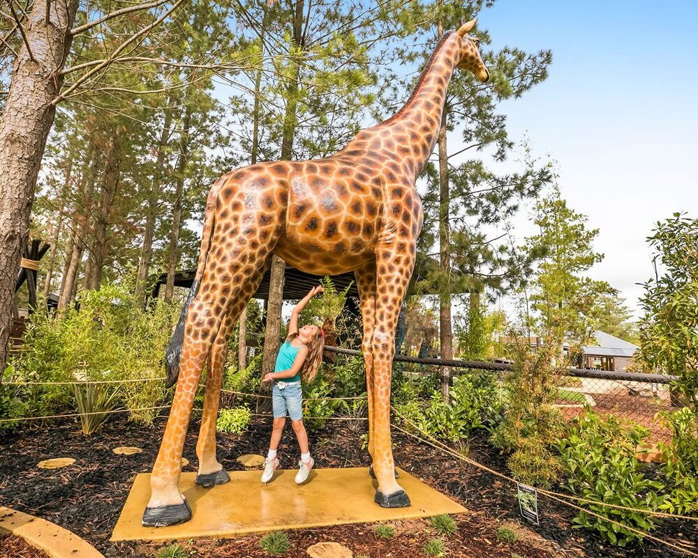 Girl under giraffe sculpture
